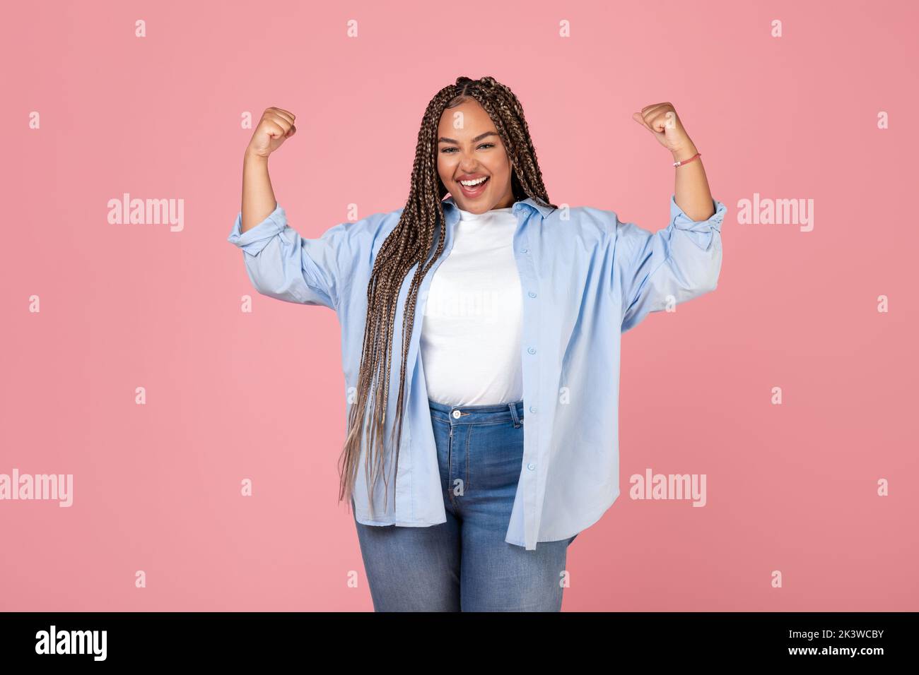 Happy Black obese femmina che mostra i muscoli bicipiti su sfondo rosa Foto Stock