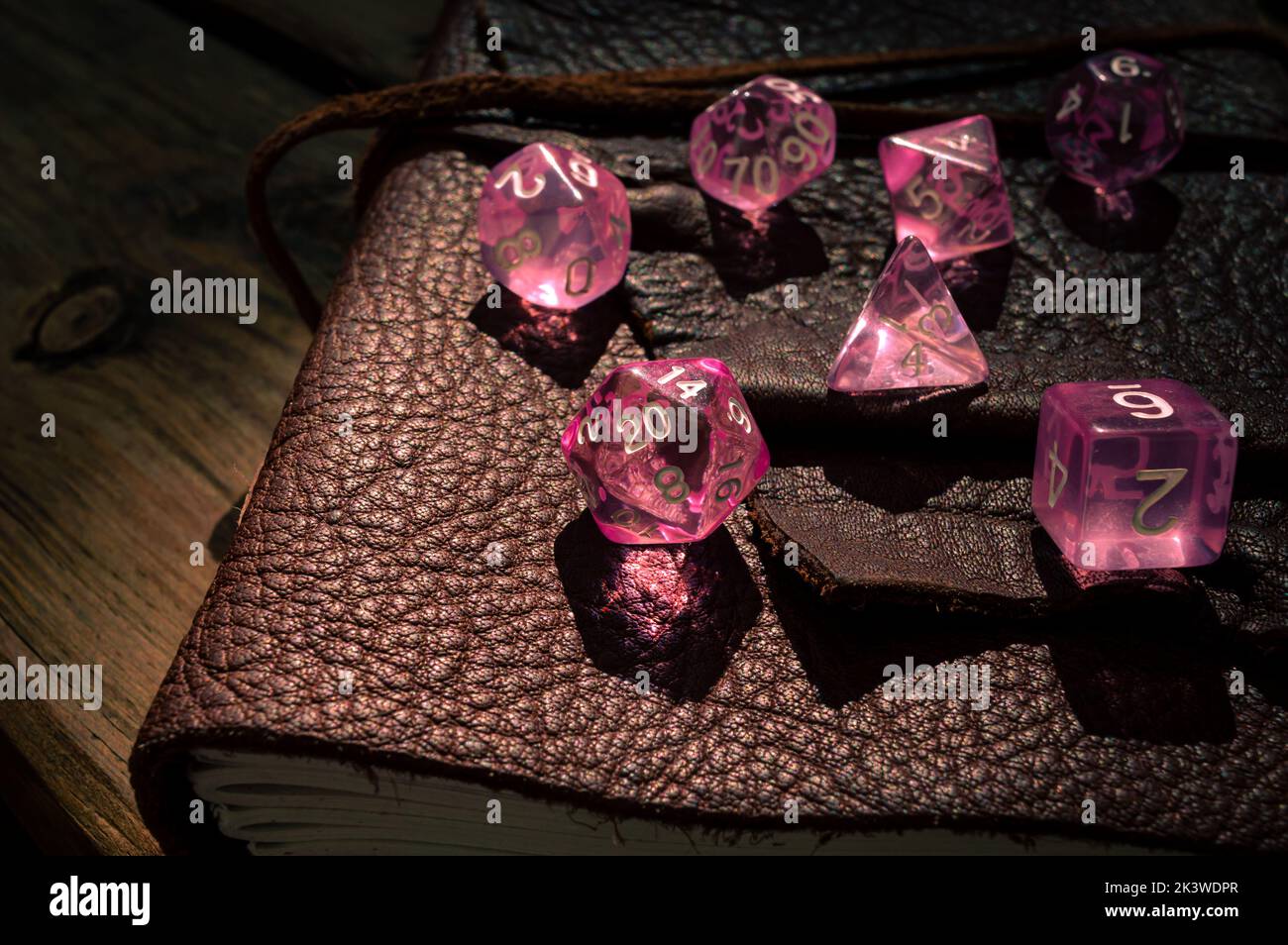 Immagine di un set di dadi RPG rosa trasparenti su un notebook con rilegatura in pelle Foto Stock