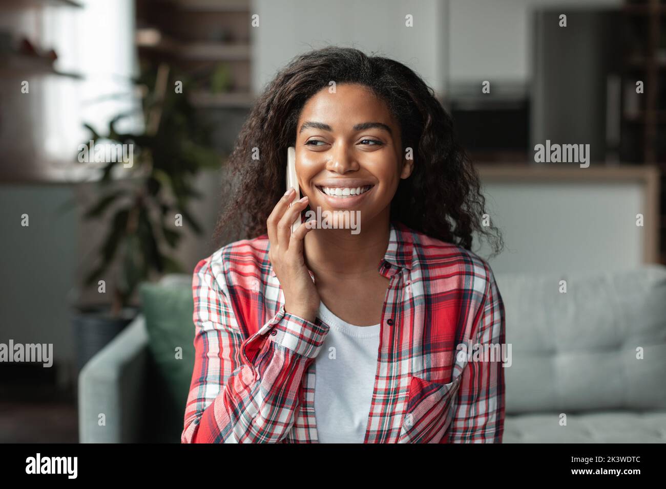 Sorridente ragazza afroamericana millenaria parla al telefono, rilassarsi sul divano, godersi il tempo libero nel soggiorno Foto Stock