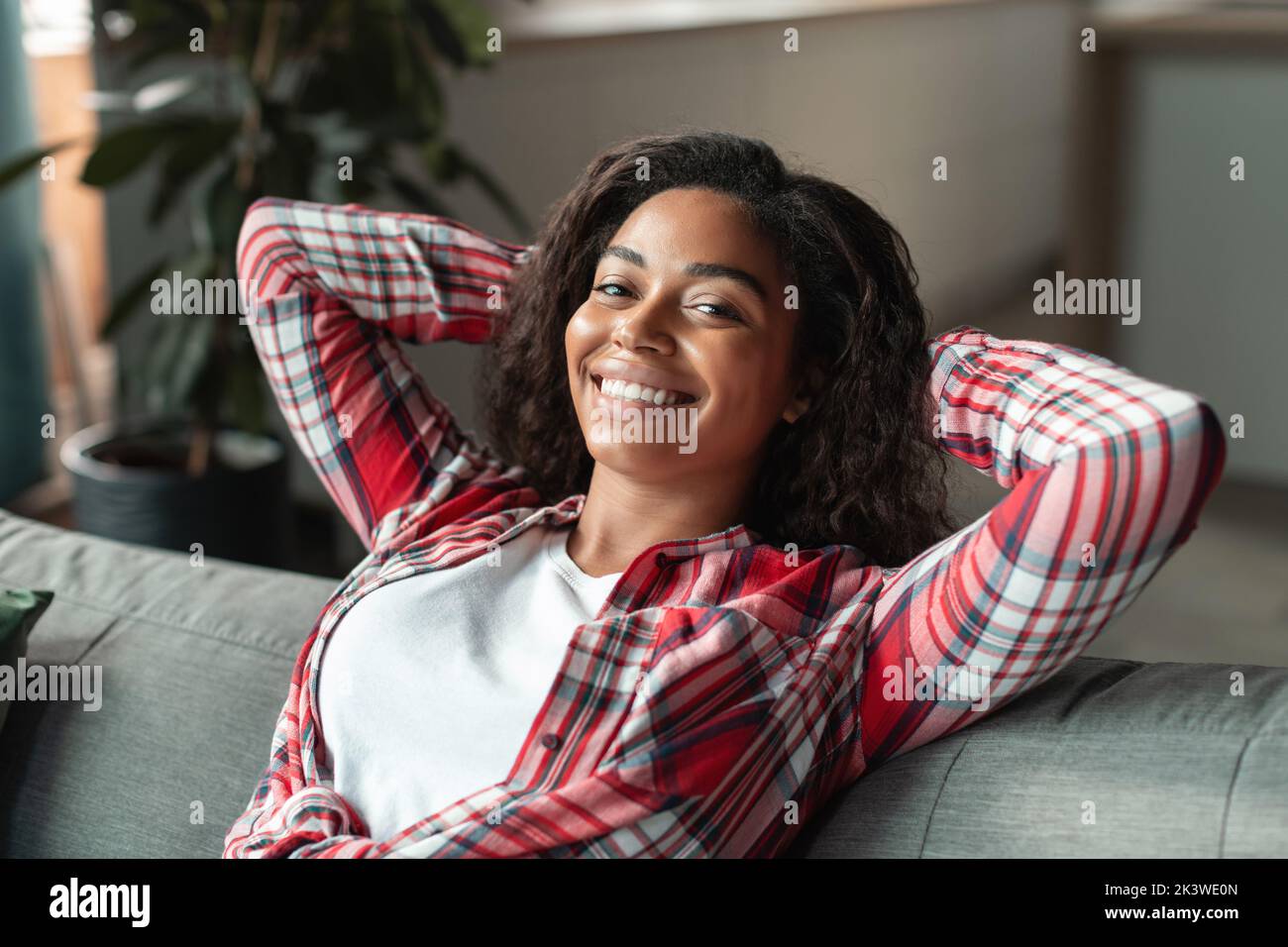 Ritratto di allegra ragazza afro-americana millenaria che si rilassa sul divano, godendosi del tempo libero nel soggiorno Foto Stock