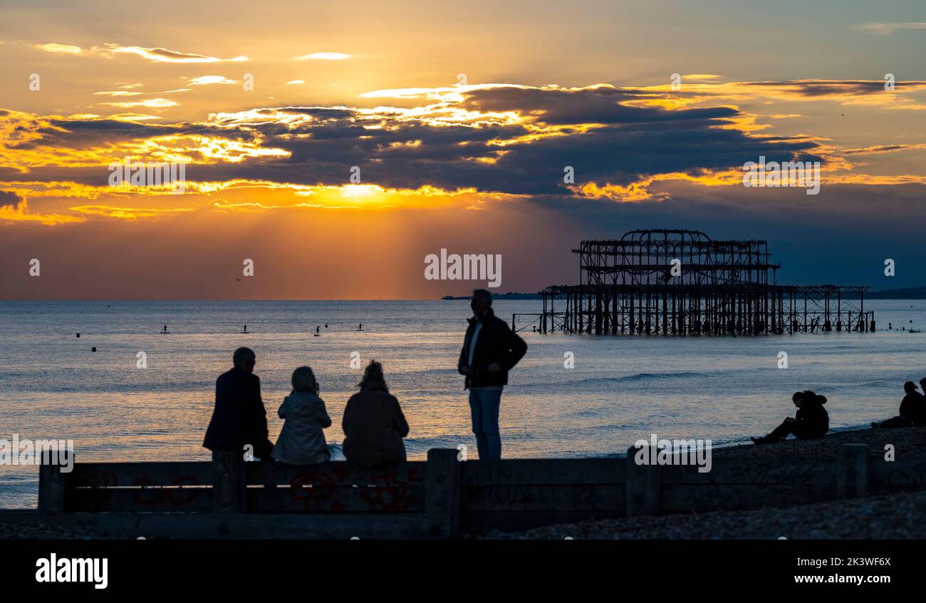 Brighton UK 28th settembre 2022 - i visitatori guardano il tramonto dietro il West Pier sul lungomare di Brighton dopo una bella giornata autunnale lungo la South Coast . Tuttavia il tempo umido e ventoso è previsto per arrivare il Venerdì nel Regno Unito . : Credit Simon Dack / Alamy Live News Foto Stock