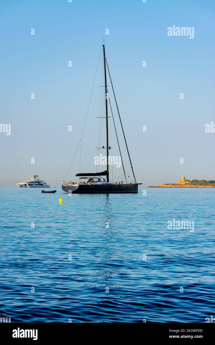 Uno yacht e una barca a vela ormeggiati con la torre di Ses Illetes a Palma di Maiorca, Spagna Foto Stock