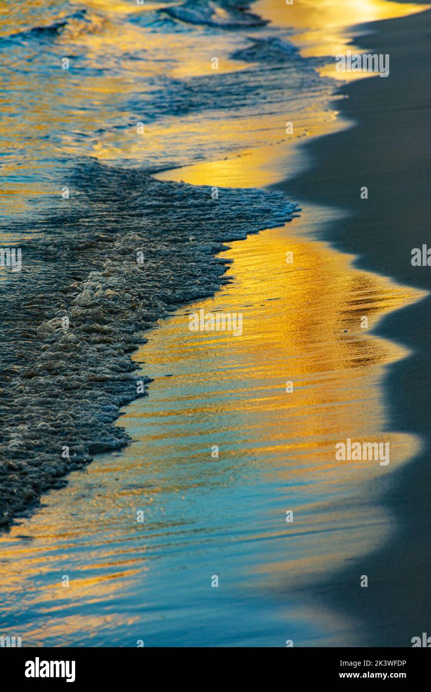 Sabbia bagnata da un'onda di bolle sulla riva della spiaggia con riflessi luminosi di alba o tramonto Foto Stock