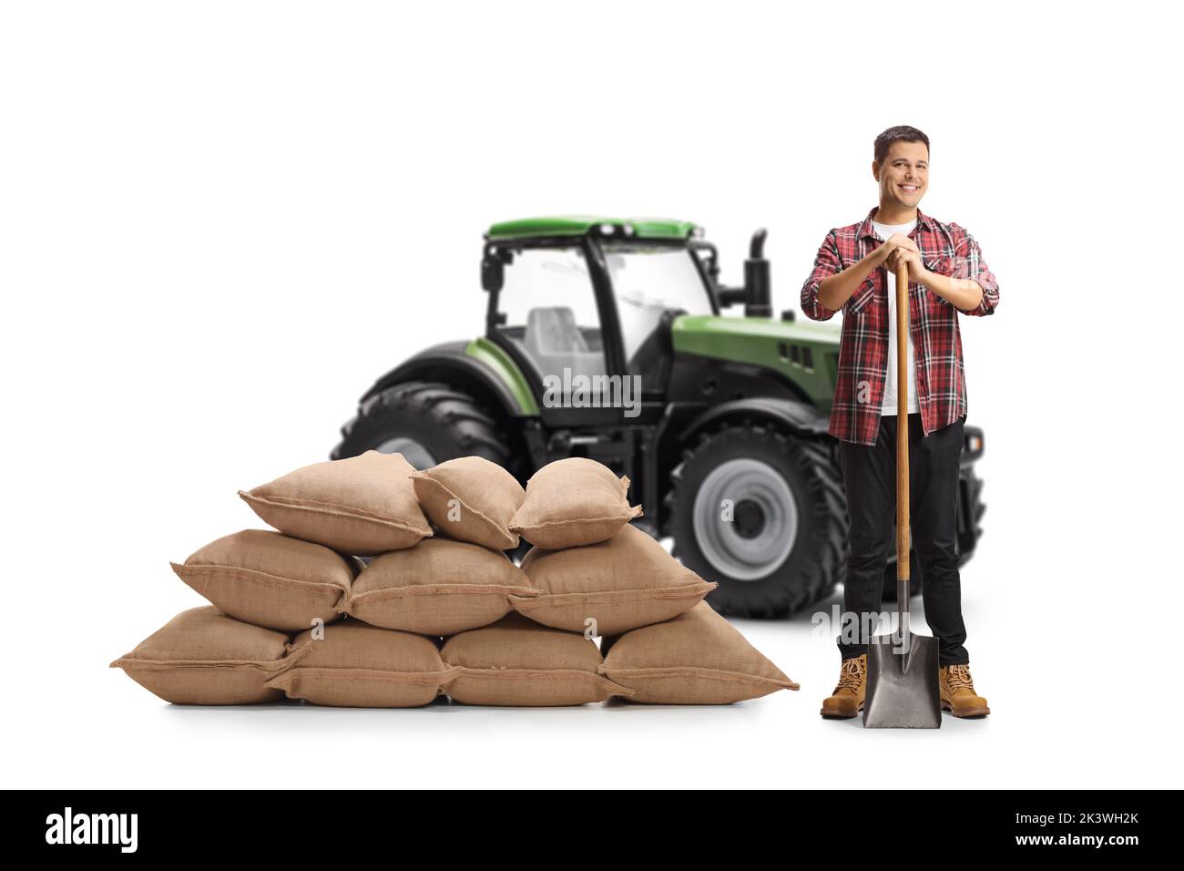 Ritratto completo di un agricoltore maschio con una pala in piedi davanti a un trattore isolato su sfondo bianco Foto Stock