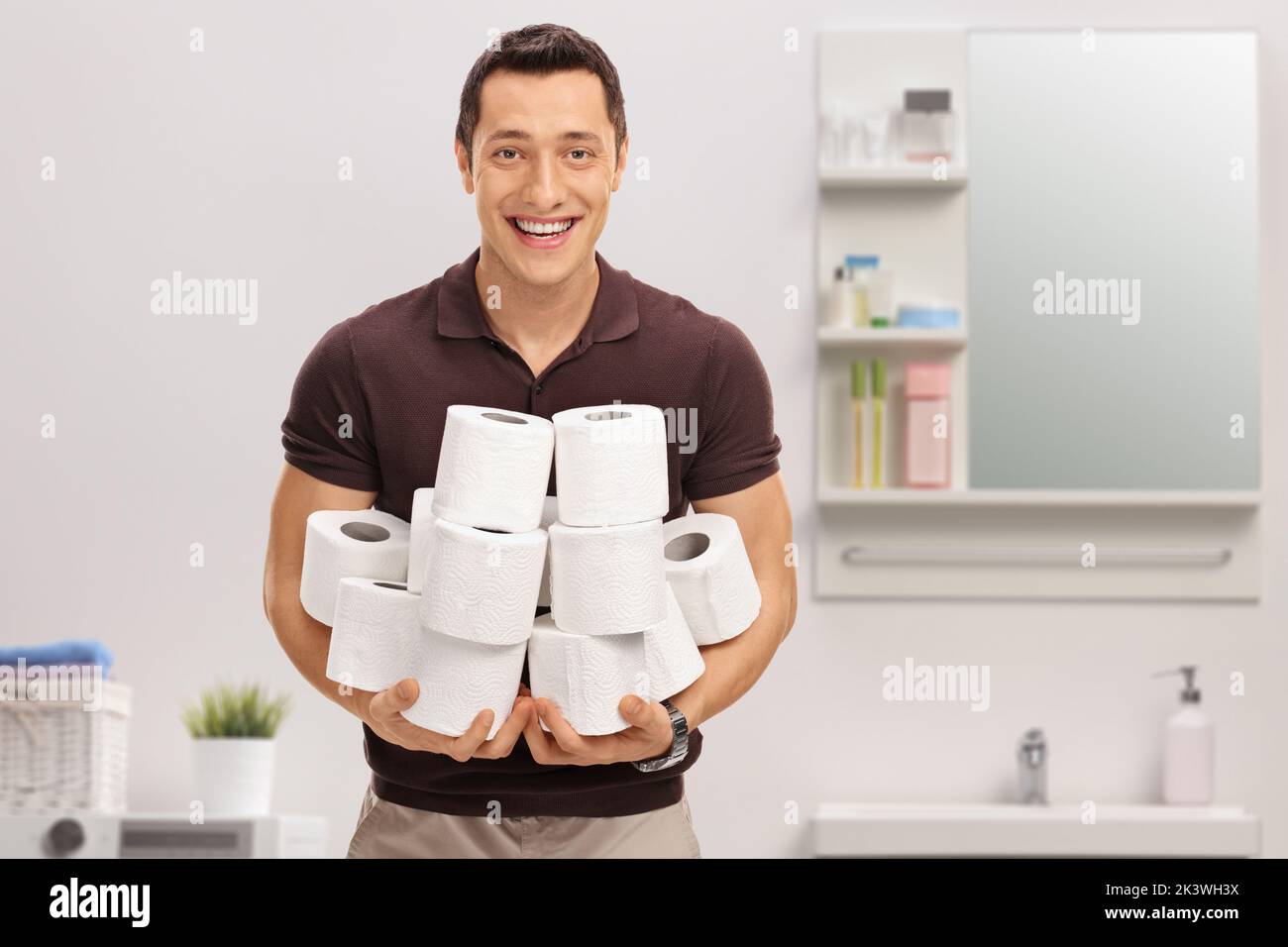 Giovane uomo sorridente che tiene un mucchio di rotoli di carta igienica all'interno del bagno Foto Stock