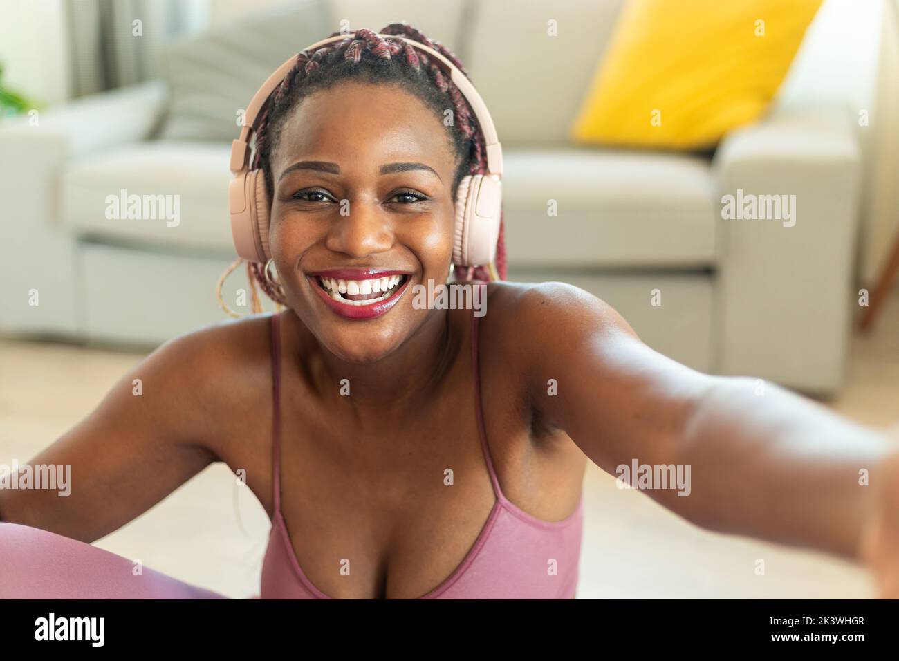 Donna nera allegra che prende selfie in pausa dall'allenamento di casa, indossa le cuffie e sorride alla fotocamera Foto Stock