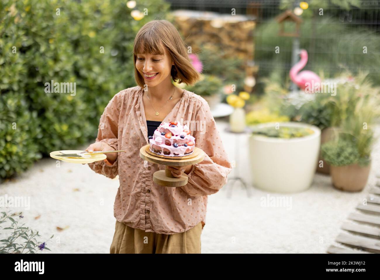 Donna con torta di festa in giardino Foto Stock