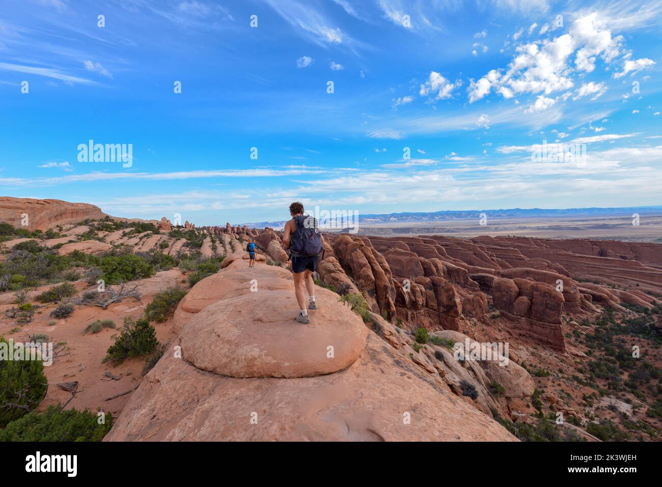 Persone che camminano lungo un sentiero in cima all'arenaria con vista speculare nel Parco Nazionale Arches nello Utah USA Foto Stock