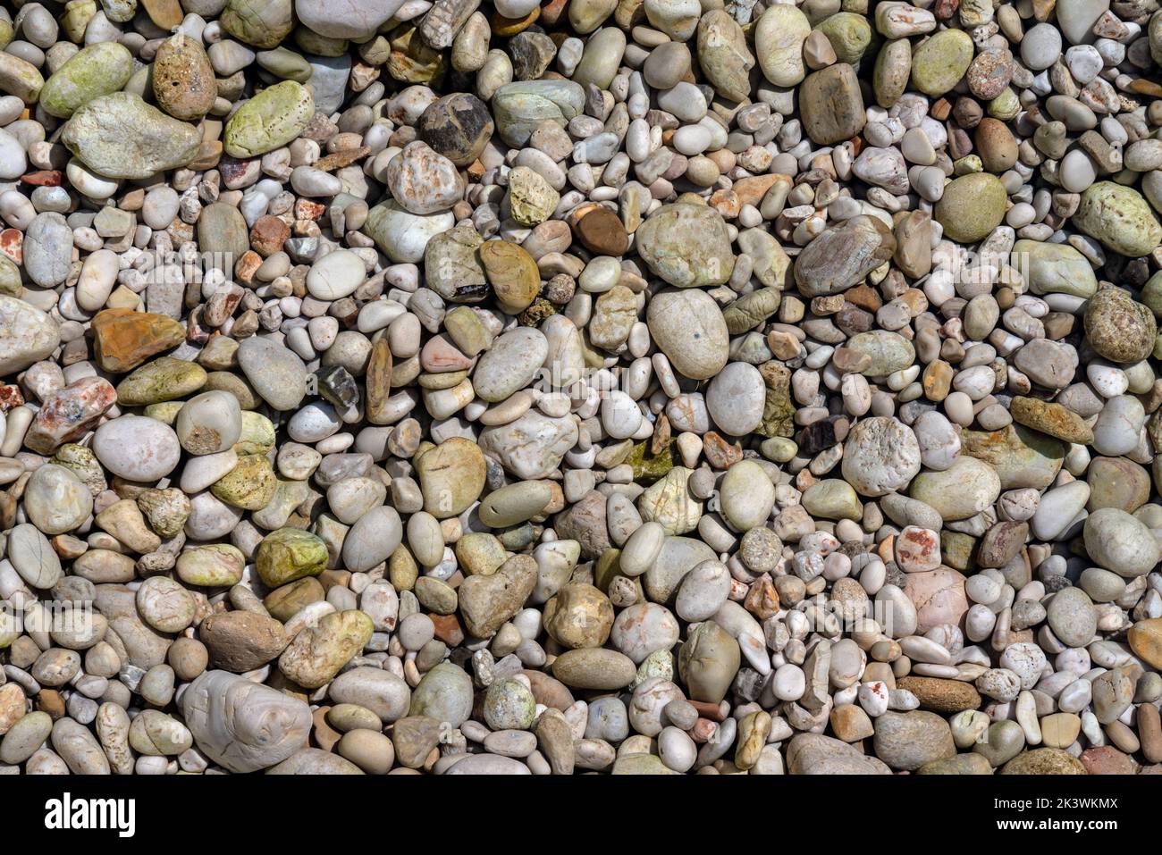 Il sole splende su piccole pietre di ghiaia alla spiaggia di Limni a Corfù, Grecia - il mare è cristallino qui - le rocce nella foto sono in realtà sotto acque poco profonde Foto Stock