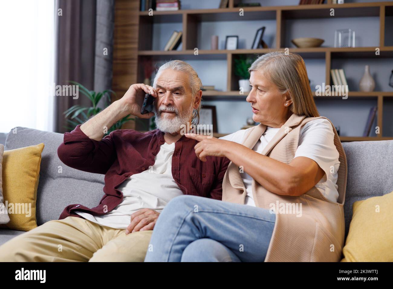 La coppia matura si siede ansiosamente a casa. Il marito dai capelli grigi riceve cattive notizie al telefono. Rapporti tra le persone anziane Foto Stock