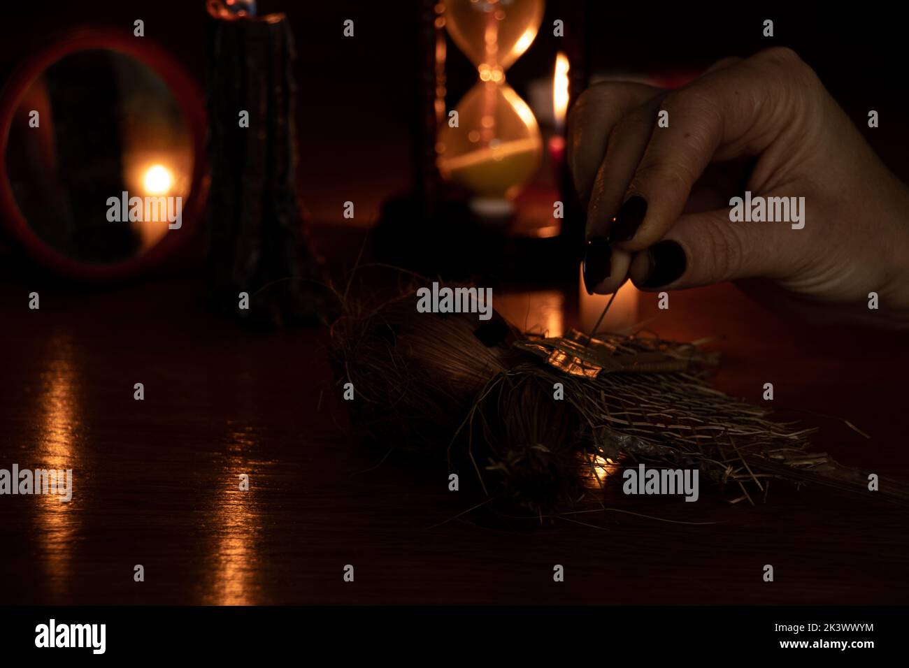 Voodoo bambola nelle mani di una strega con un ago nel suo cuore al buio sullo sfondo di candele, una maledizione e magia nera Foto Stock