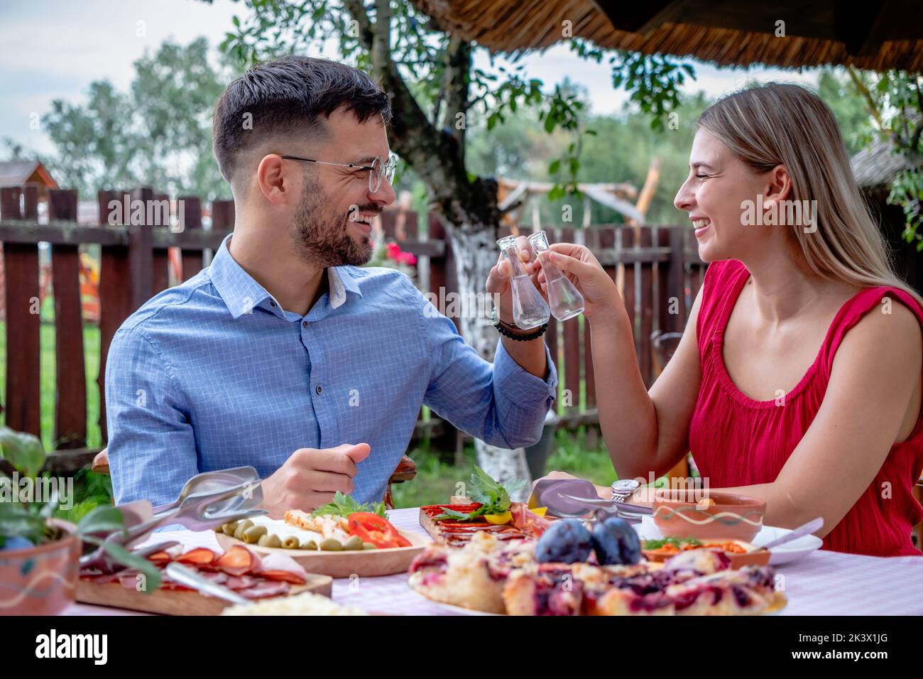Felice giovane coppia romantica brindisi con shot di brandy con un particolare collo stretto bicchieri in un bel ristorante di campagna tradizionale all'aperto. Foto Stock