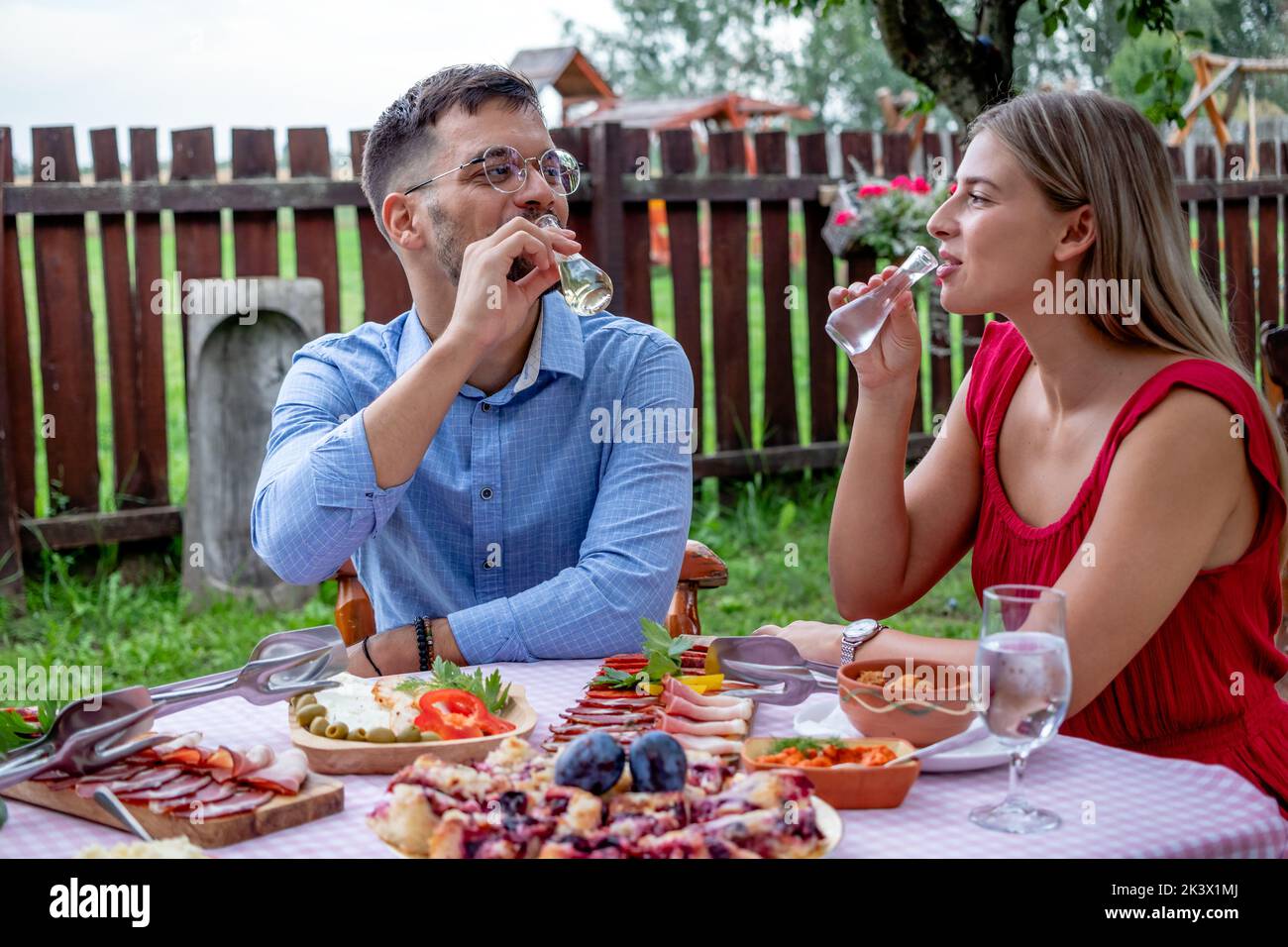 Felice giovane coppia romantica brindisi con shot di brandy con un particolare collo stretto bicchieri in un bel ristorante di campagna tradizionale all'aperto. Foto Stock