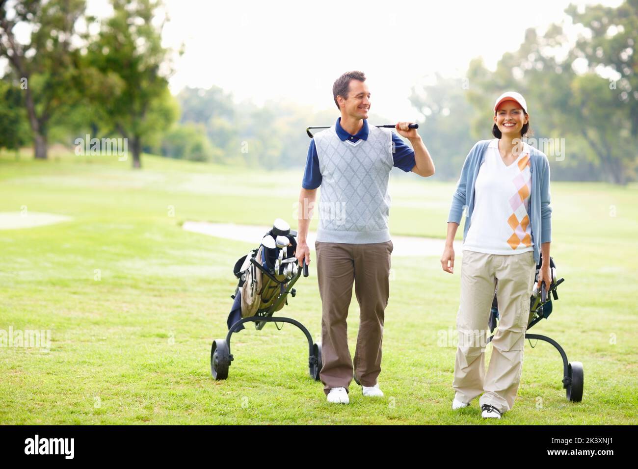 Coppia a piedi sul campo da golf. Lunghezza intera di coppia che cammina sul campo da golf con le borse da golf. Foto Stock