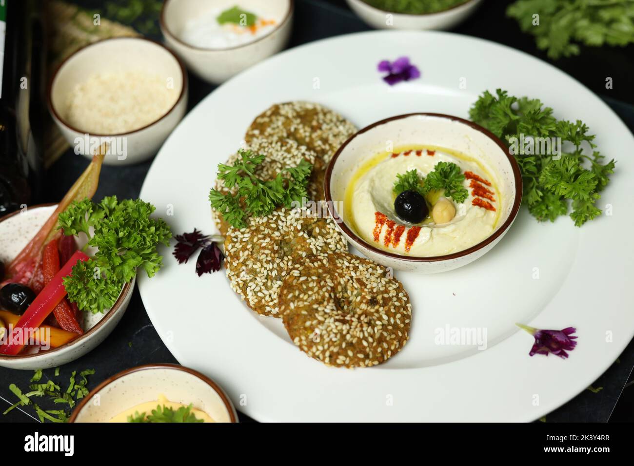 Ciotola di hummus fatta in casa, decorata con ceci bolliti, erbe aromatiche, pita e olio d'oliva su un fondo rustico di metallo Foto Stock