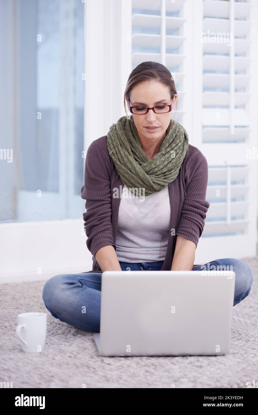 Blogging è il mio commercio. Una giovane donna che sorride mentre si siede sul pavimento e lavora sul suo notebook. Foto Stock