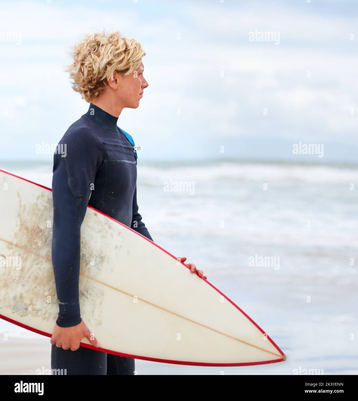 È sempre una buona giornata per fare surf. Un giovane surfista in piedi sulla spiaggia con l'oceano sullo sfondo. Foto Stock