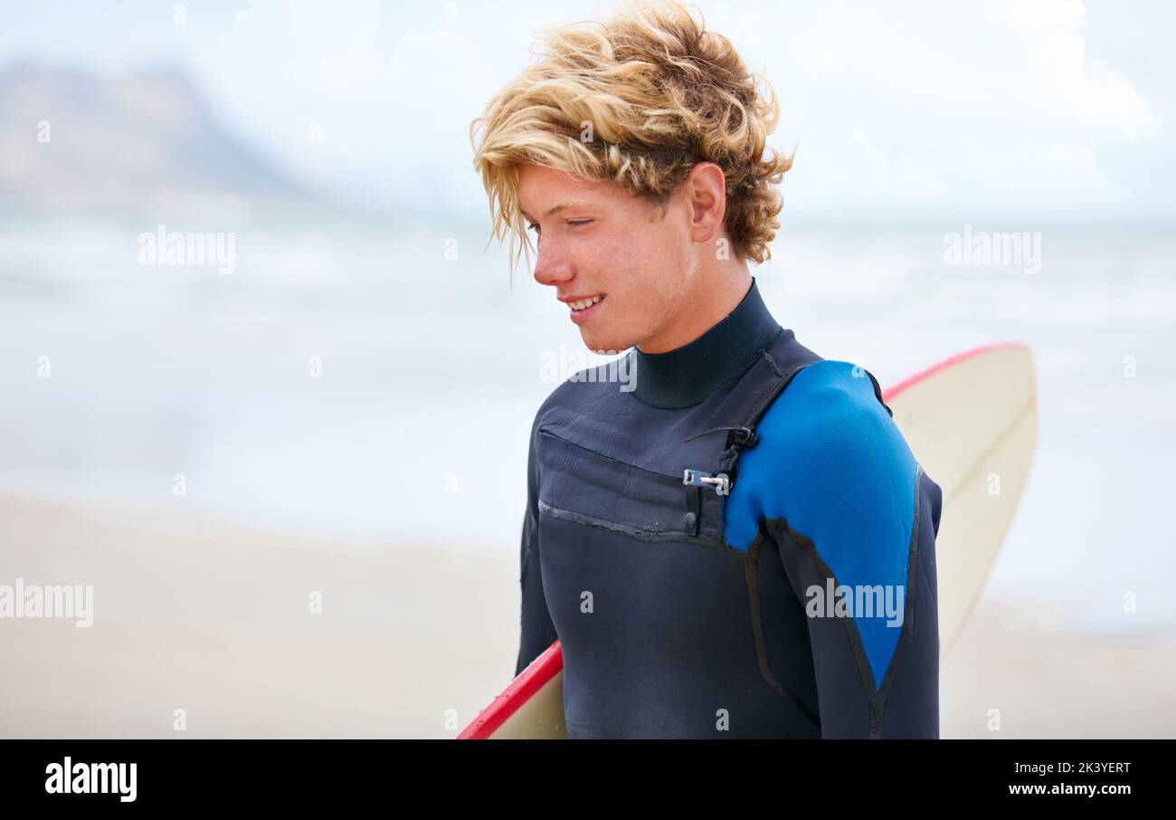 Alla ricerca di quell'onda perfetta... Un giovane surfista in piedi sulla spiaggia con l'oceano sullo sfondo. Foto Stock