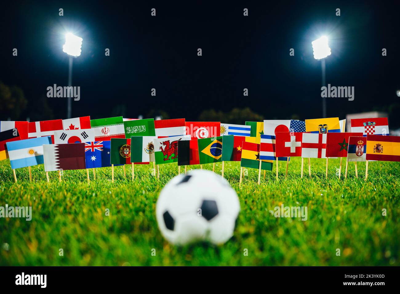 Palla di calcio su erba verde e tutte le 32 bandiere nazionali. Gioco di calcio, carta da parati con spazio di modifica nero. Torneo di calcio e stadio Foto Stock