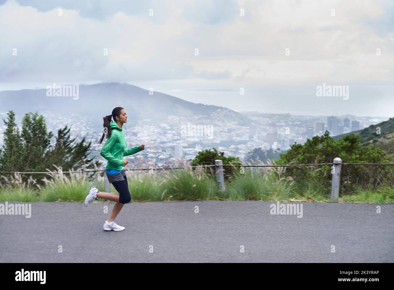 Progredisce nella sua idoneità giornaliere. Una giovane donna che si snoda lungo una strada di montagna in una mattinata frizzante. Foto Stock