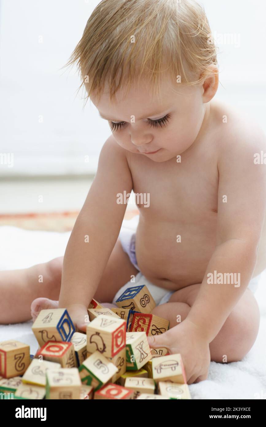 Mostrare interesse nei giochi educativi. Un bambino che gioca con i suoi blocchi di costruzione che osservano il soddisfare. Foto Stock