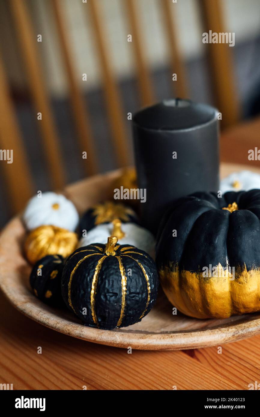 Decorazioni in stile halloween con zucca nera. Composizione decorativa moderna e minimale per interni con zucche nere dorate in piatto di legno a tavola Foto Stock