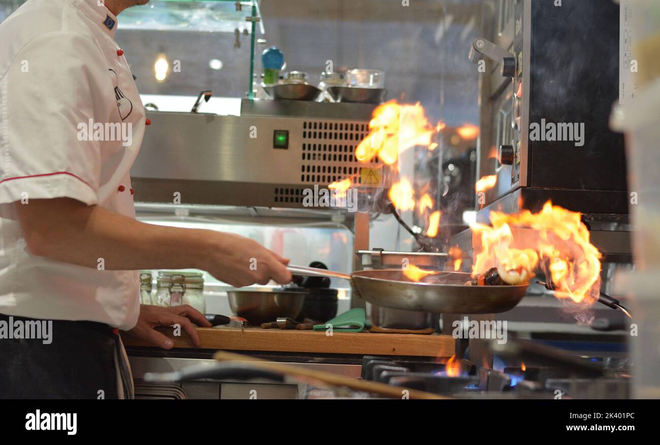Frutti di mare cucinati con fiamma in una cucina professionale. Lo chef è fotografato da un lato. Foto Stock