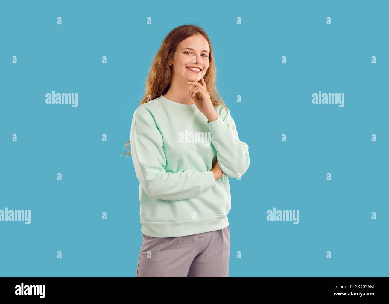 Giovane donna o ragazza adolescente in felpa alla menta leggera che posa su sfondo blu studio Foto Stock