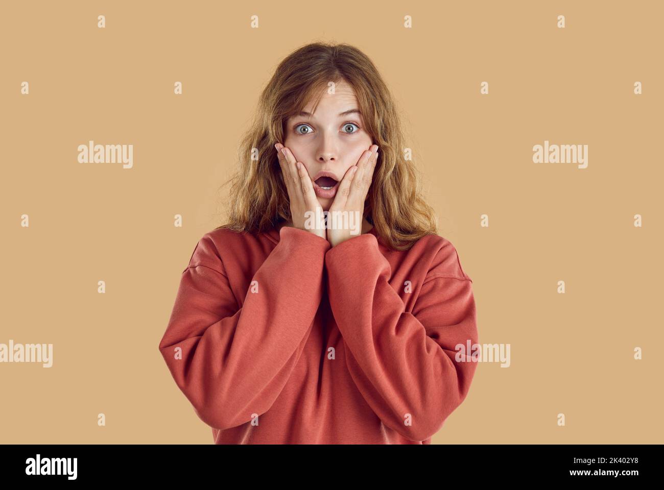 Ritratto di giovane donna stupita con gli occhi spalancati e la bocca aperta con le mani sul viso. Foto Stock