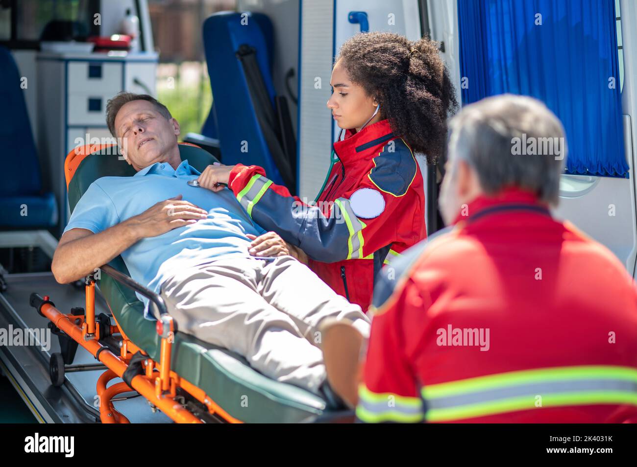Paramedico che esamina un uomo inconscio sdraiato sulla barella Foto Stock