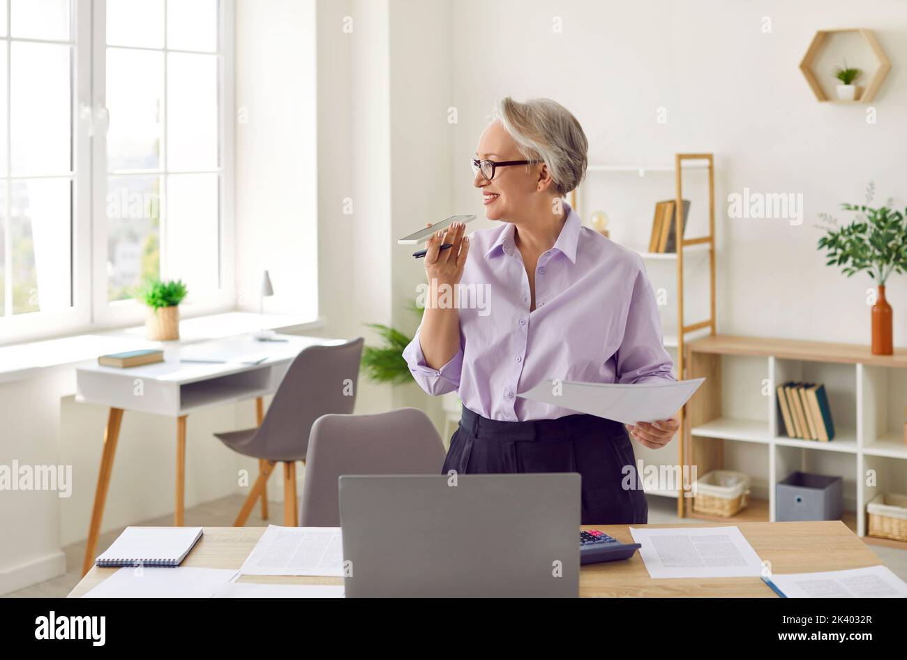 La donna d'affari senior in ufficio utilizza la funzione di riconoscimento vocale o un assistente virtuale sul telefono cellulare. Foto Stock