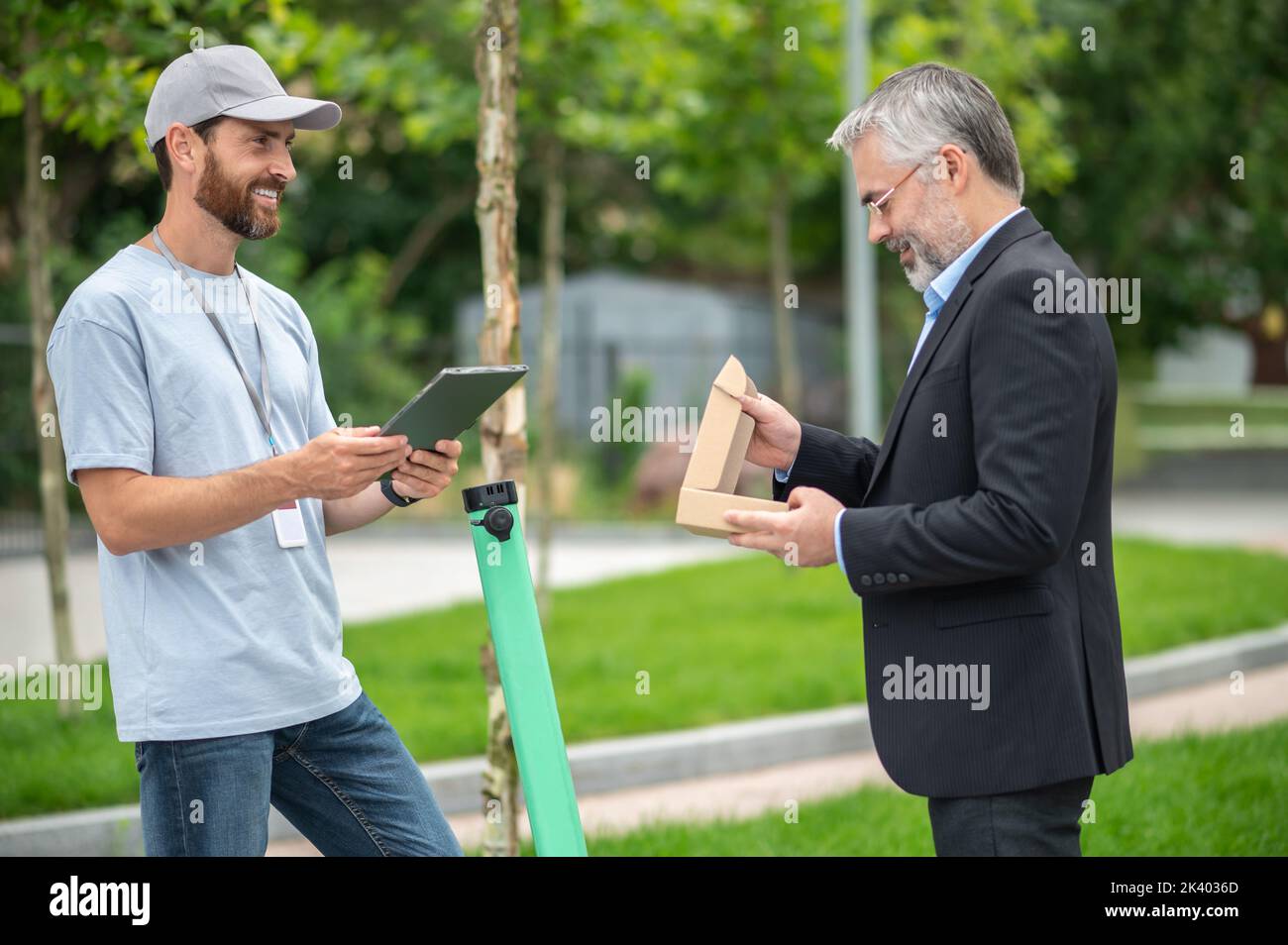 Uomo d'affari che riceve una scatola di consegna dal corriere su uno scooter Foto Stock