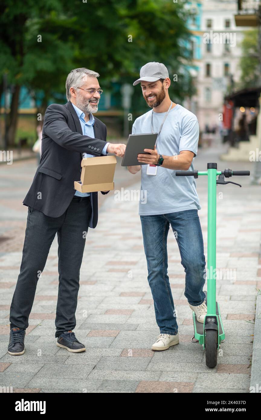 Uomo d'affari che riceve una scatola di consegna dal corriere su uno scooter Foto Stock