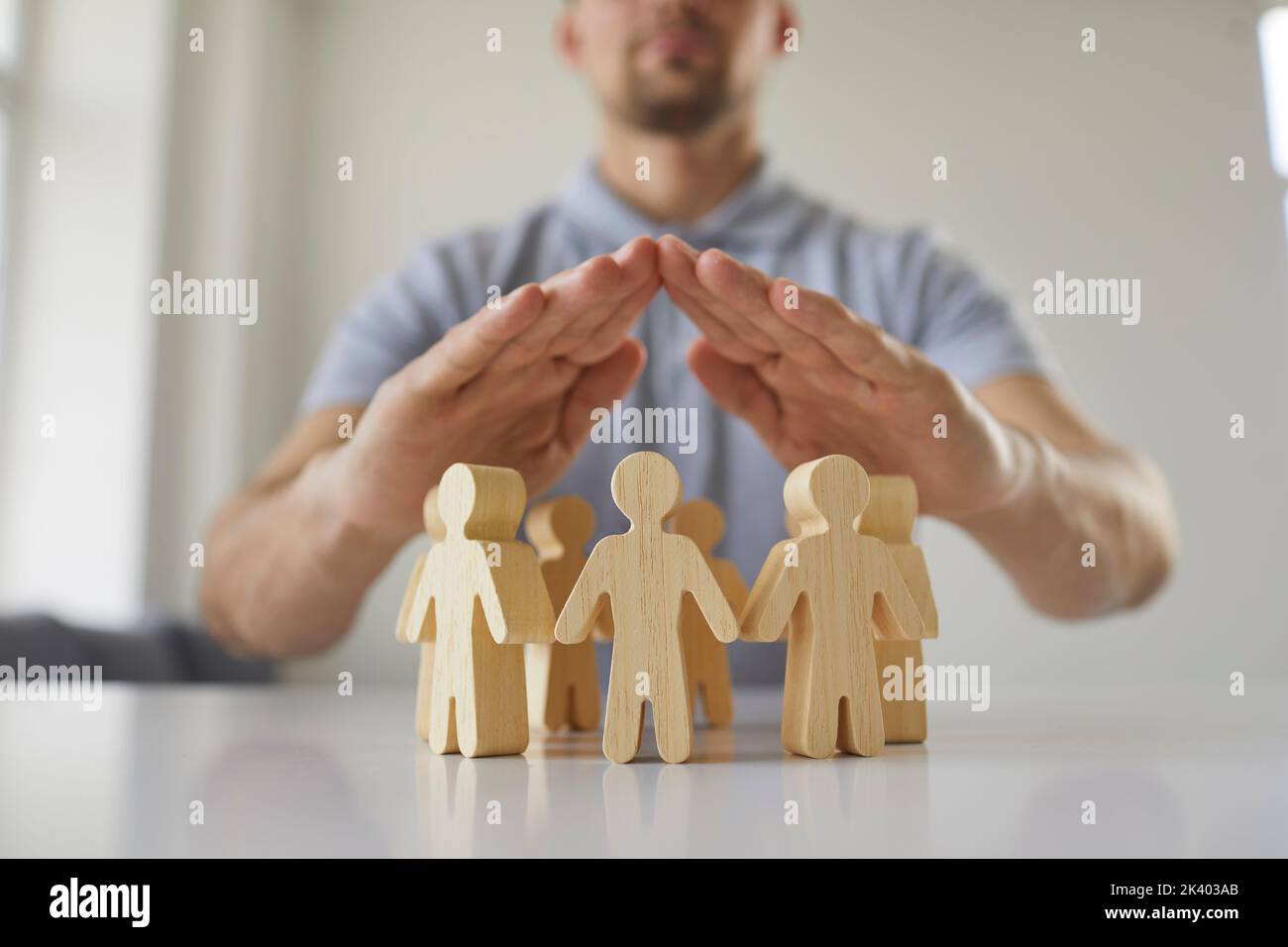 Uomo che tiene le mani sopra figure umane di legno come metafora per la sicurezza e la protezione Foto Stock