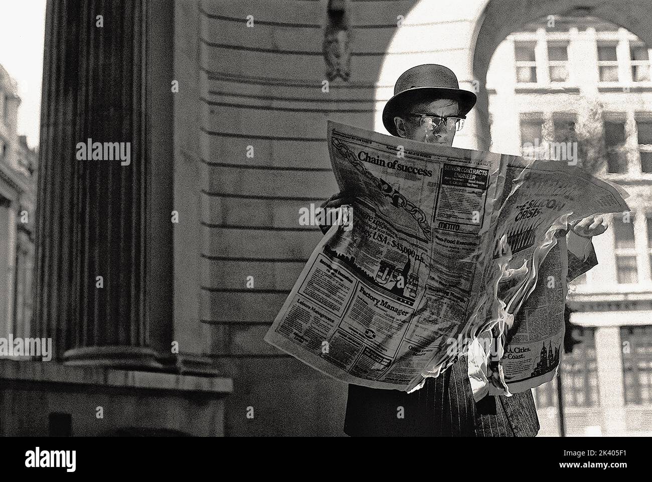 Un uomo d'affari vecchio stile che tiene un giornale che è sul fuoco, che brucia. Foto Stock