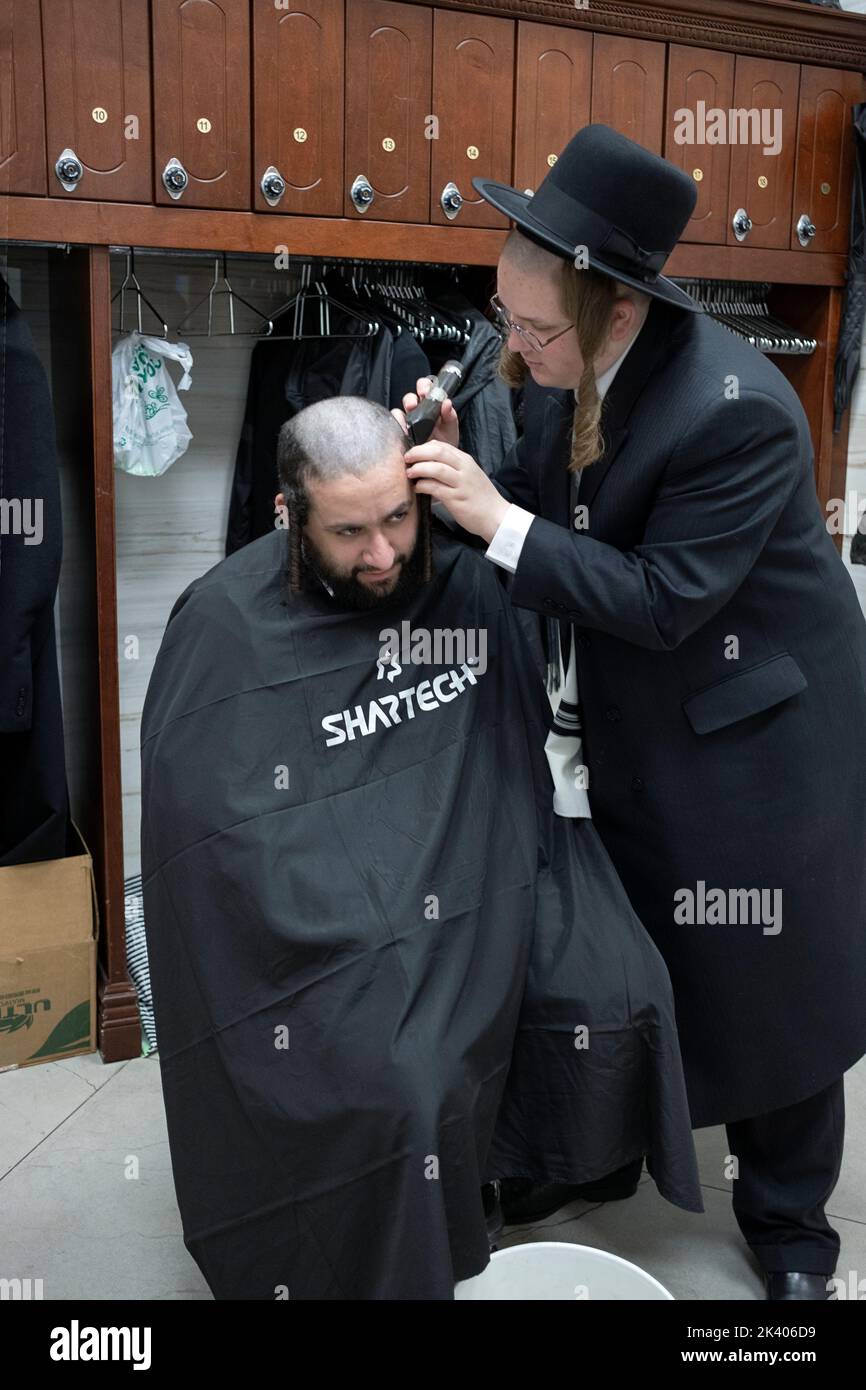 Un taglio di capelli chassidico osservando il passaggio in Levitico dicendo che gli ebrei non dovrebbero "tagliare gli angoli della loro barba". In una sinagoga a New York. Foto Stock