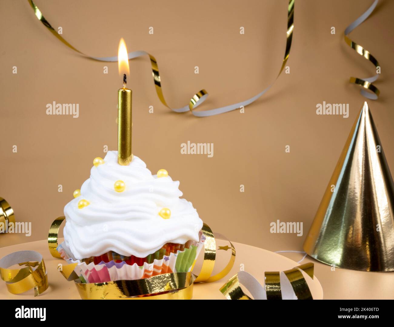 Torta di compleanno o cupcake con una candela dorata bruciante su uno sfondo beige. Il concetto di celebrare una festa, anniversari in colori dorati. Foto Stock