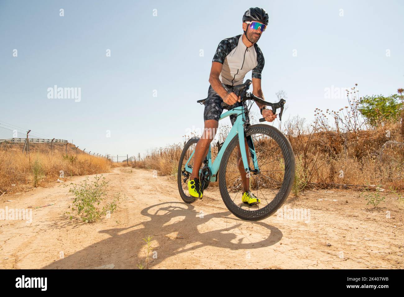 Ciclista pedalando la sua bici da corsa all'aperto con tutte le sue attrezzature di sicurezza: Casco, occhiali da sole, in una giornata di sole Foto Stock