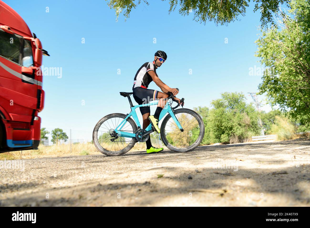Il ciclista si è fermato sulla sua moto da corsa su strada con tutte le sue attrezzature di sicurezza: Casco, occhiali da sole, sicurezza. Con un camion che passa Foto Stock