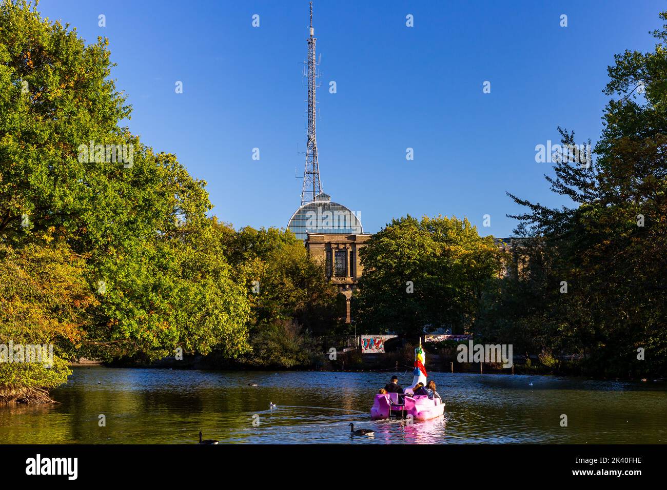 Una famiglia ebraica ortodossa che si diverta in un'insolita barca a remi sul lago Alexandra Park nel nord di Londra. La torre della BBC è chiaramente visibile. Foto Stock