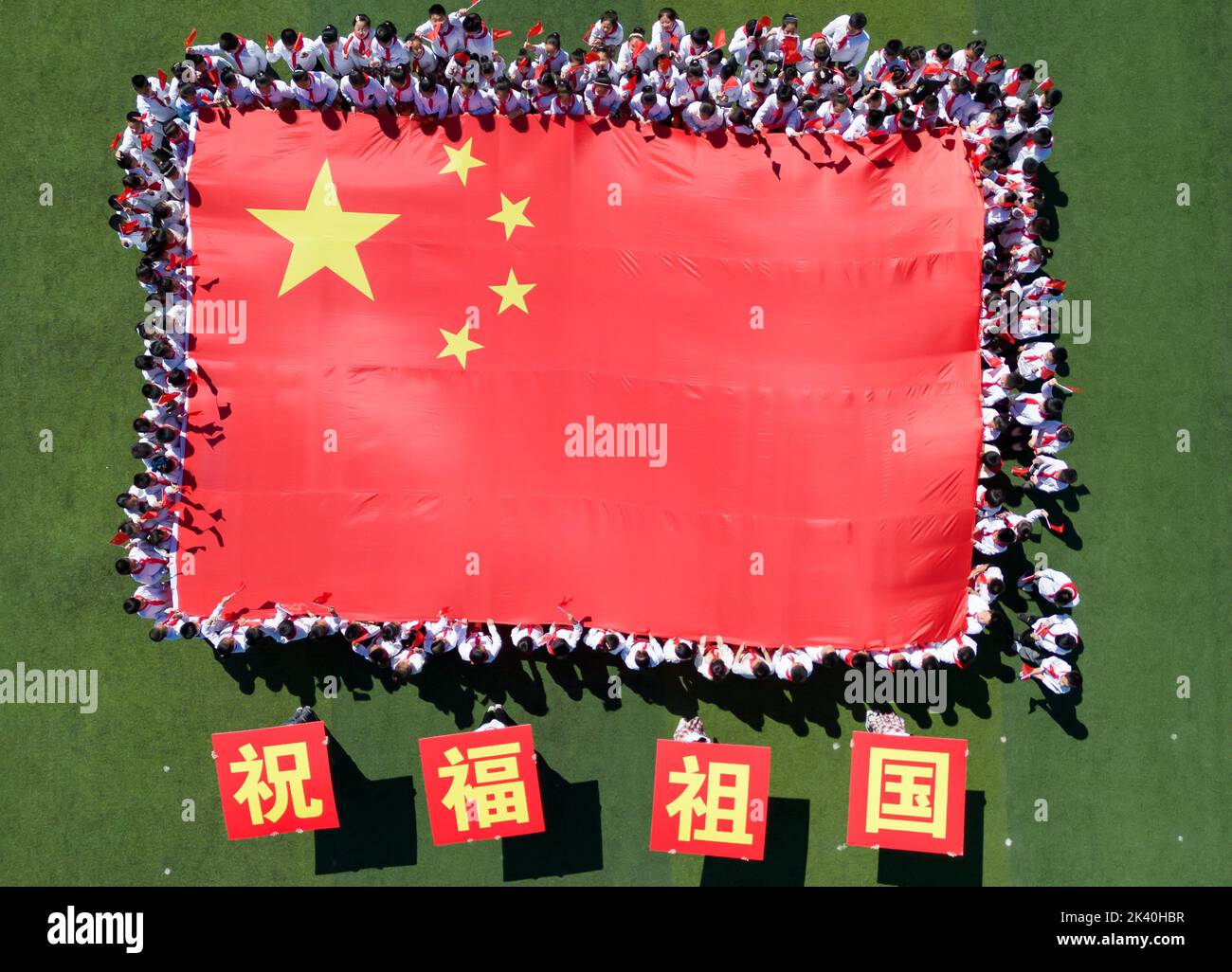 HAI'AN, CINA - 29 2022 SETTEMBRE - gli studenti delle scuole primarie posano con bandiere nazionali per celebrare il 73rd° anniversario della fondazione del popolo Foto Stock