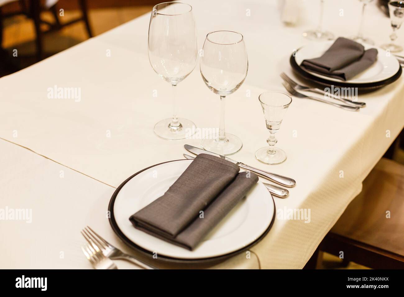 Primo piano nuovi piatti di porcellana bianca sui tappetini viola e bicchieri da vino vuoti pronti per cena. Le impostazioni del tavolo attendono gli ospiti a casa o. Foto Stock