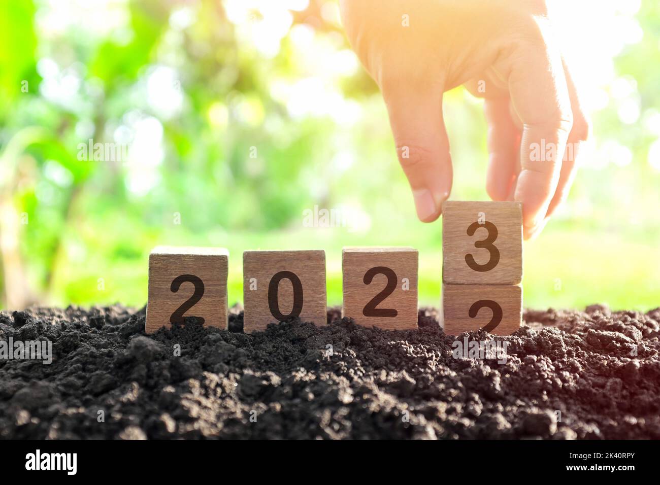 Mano che cambia anno 2022 a 2023 in blocchi di legno cubetti con pianta crescente all'alba. Anno nuovo 2023, Hope, Hello e Arrivederci Concept. Foto Stock