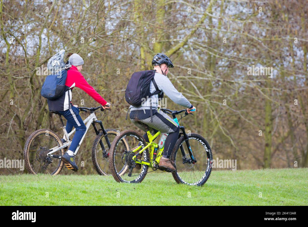 Vista laterale di due ciclisti in mountain bike con zaini in bicicletta sull'erba nel parco di campagna, Regno Unito. Foto Stock