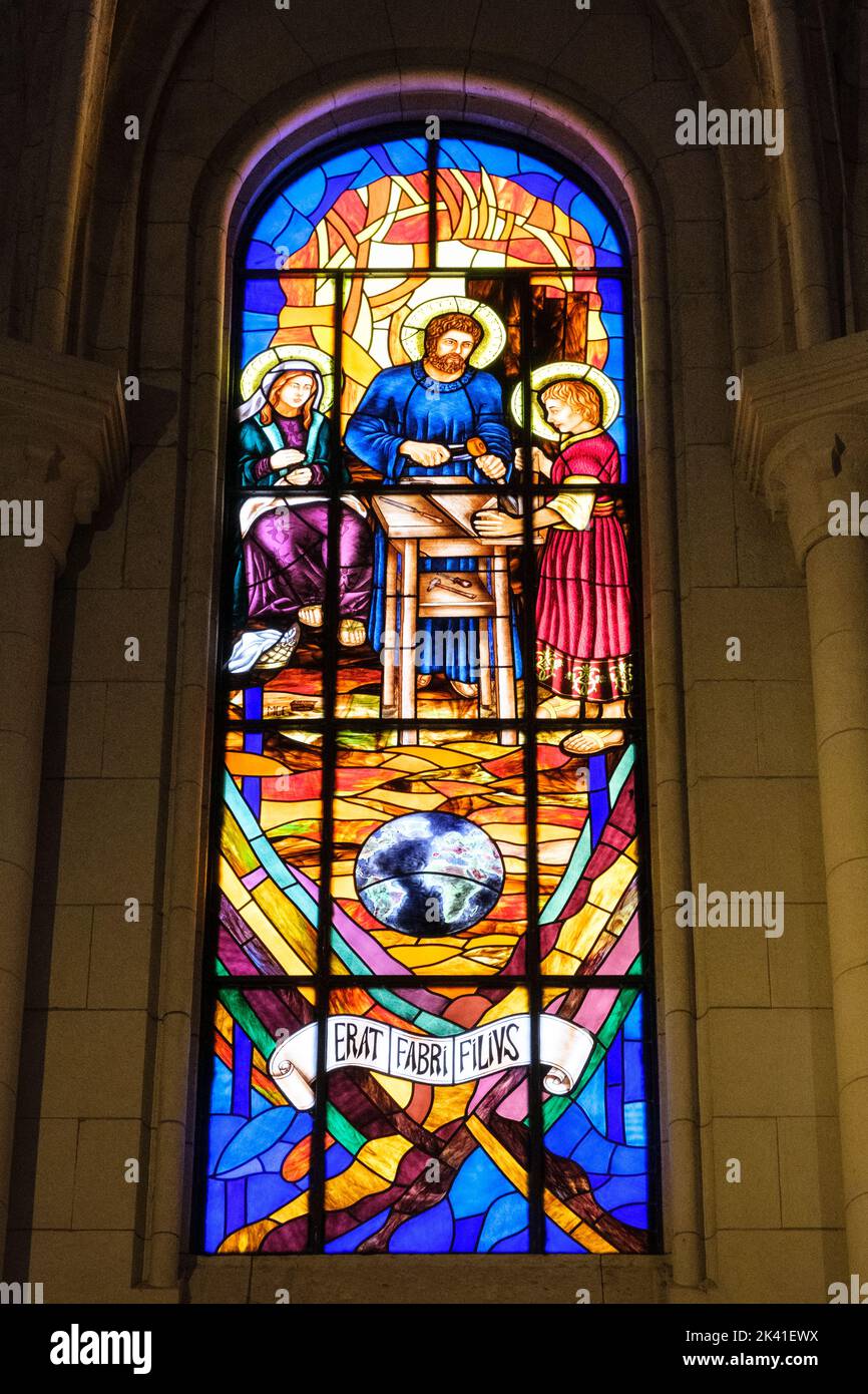 Spagna, Madrid. Cattedrale dell'Almudena. Moderna finestra di vetro colorato. 'Era figlio di un operaio' in latino. Foto Stock