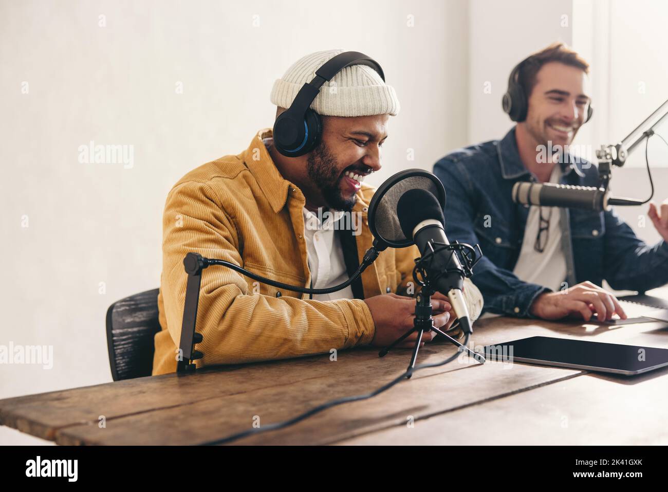 Due podcaster universitari ridono e si divertono in uno studio. Due giovani uomini felici co-ospitare una trasmissione audio dal vivo. Due creatori di contenuti maschili r Foto Stock