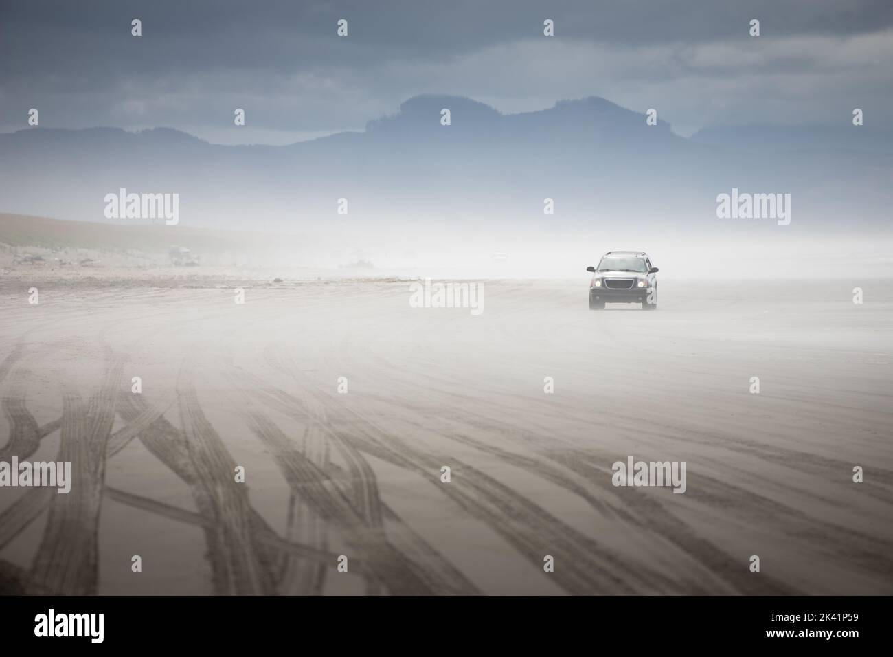 Segni di pneumatici lasciati sulla sabbia dai camion che guidano sulla spiaggia con un SUV che esce dalla nebbia Foto Stock