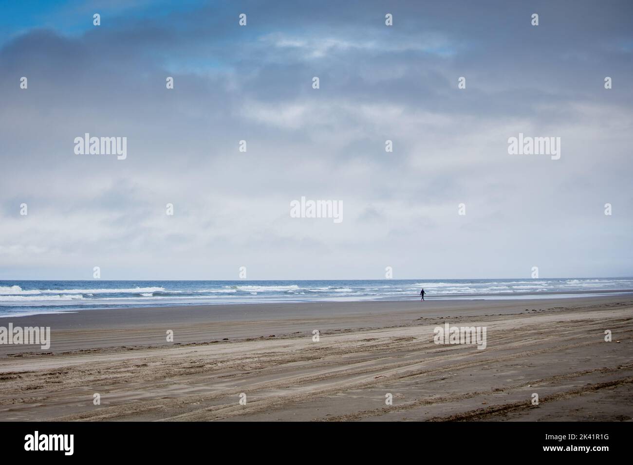 Una persona isolata che cammina lungo una spiaggia di sabbia deserta Foto Stock