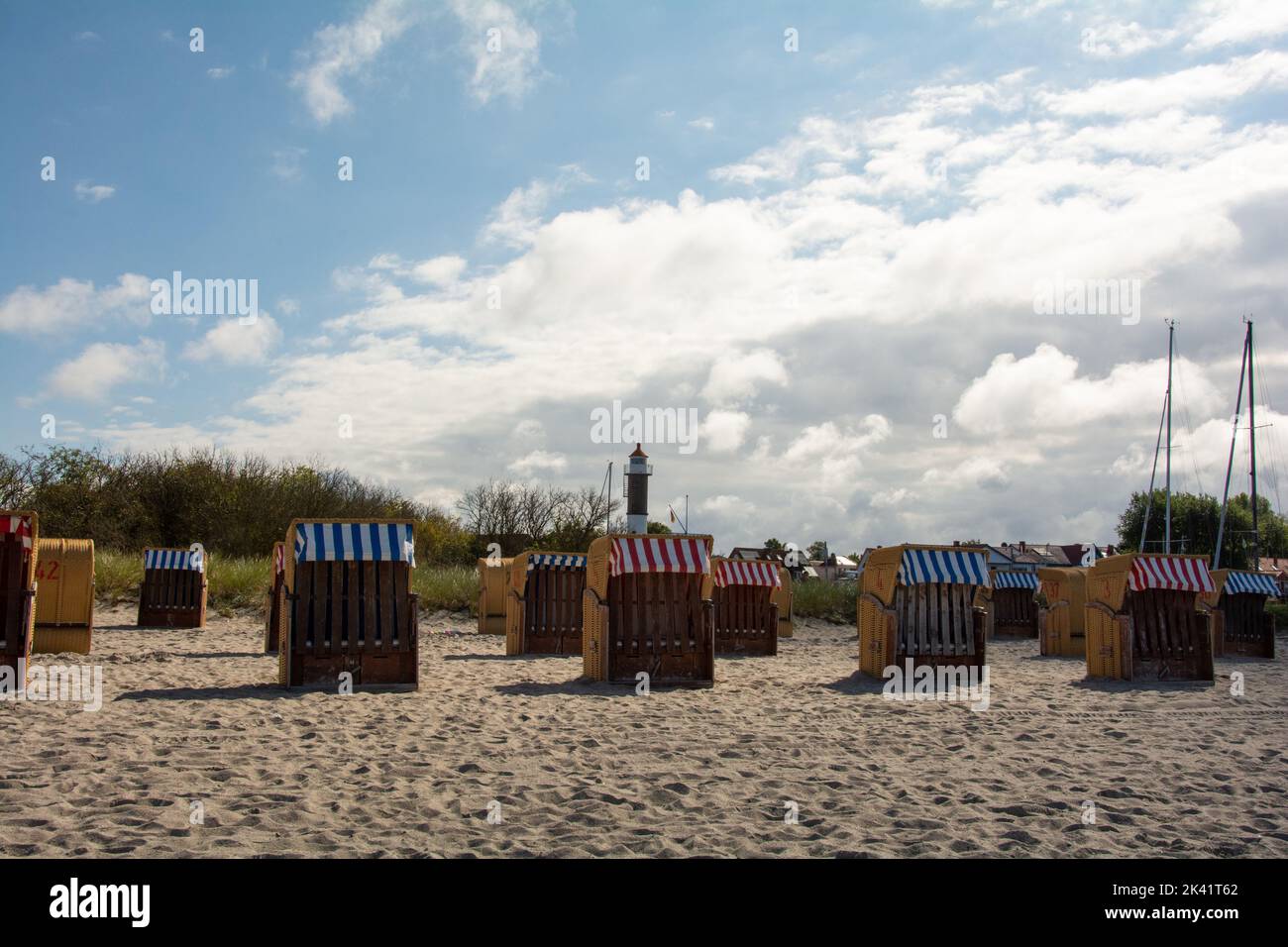 Vista sulle tradizionali sedie a sdraio marroni in vimini e sul faro sulla spiaggia sabbiosa del Mar Baltico, vicino a Timmendorf Strand, sull'isola Foto Stock