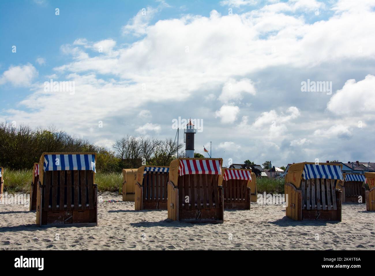 Vista sulle tradizionali sedie a sdraio marroni in vimini e sul faro sulla spiaggia sabbiosa del Mar Baltico, vicino a Timmendorf Strand, sull'isola Foto Stock